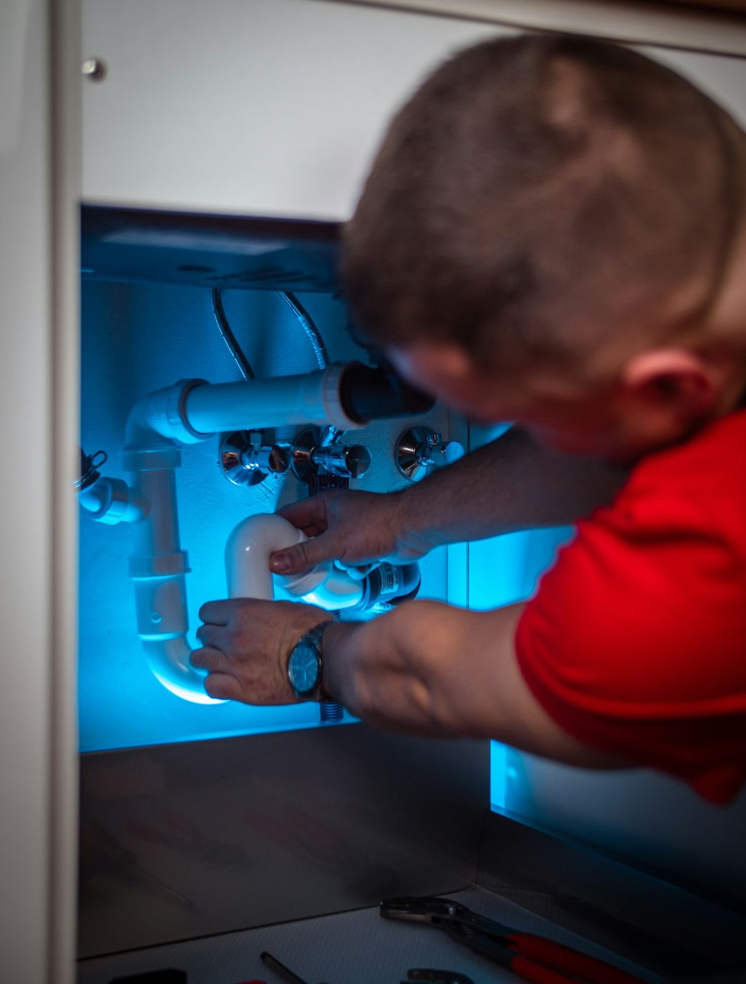 A Brightline plumber working on the pipes under a kitchen sink
