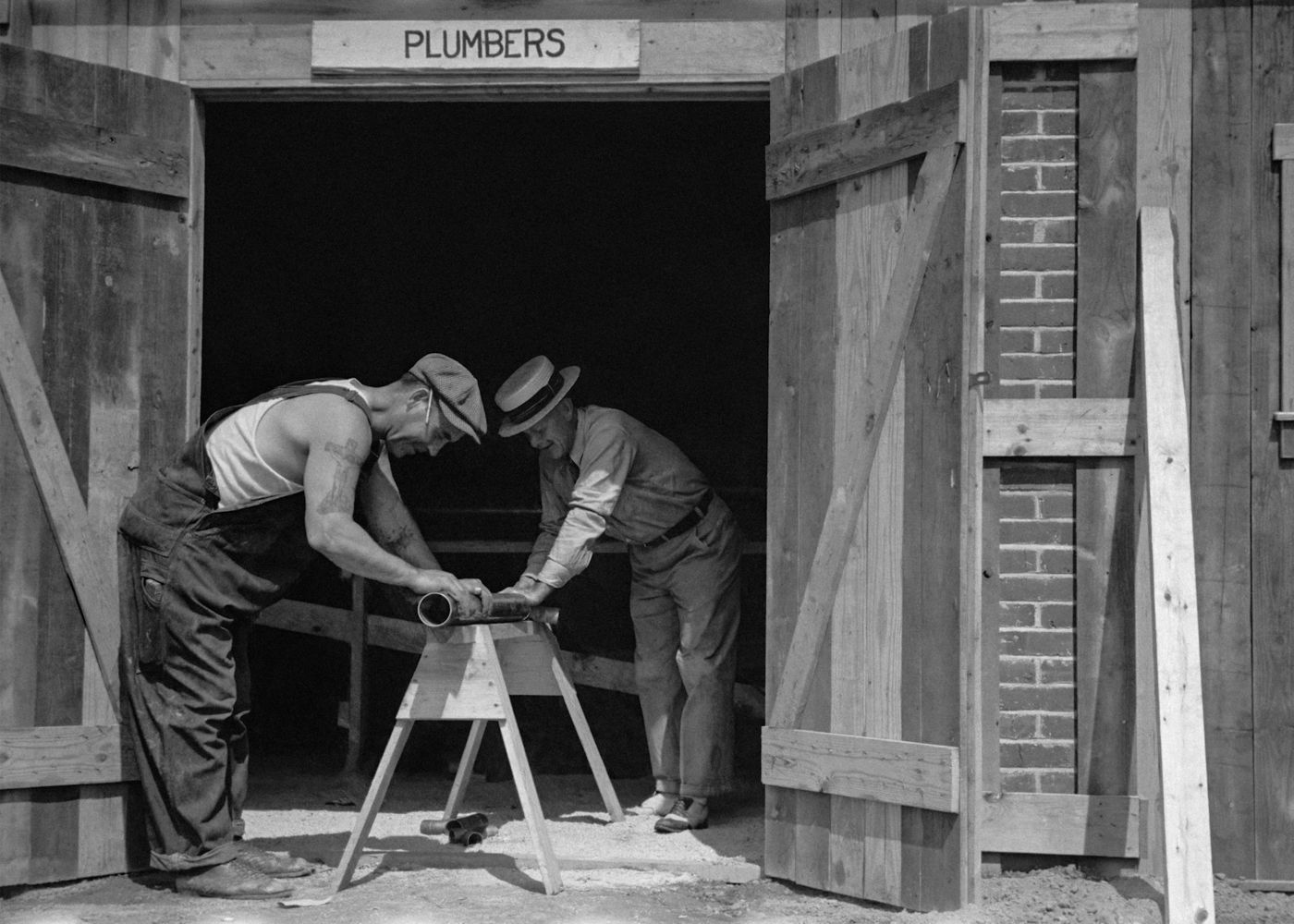 An old black and white photo of two plumbers working in a workshop doorway
